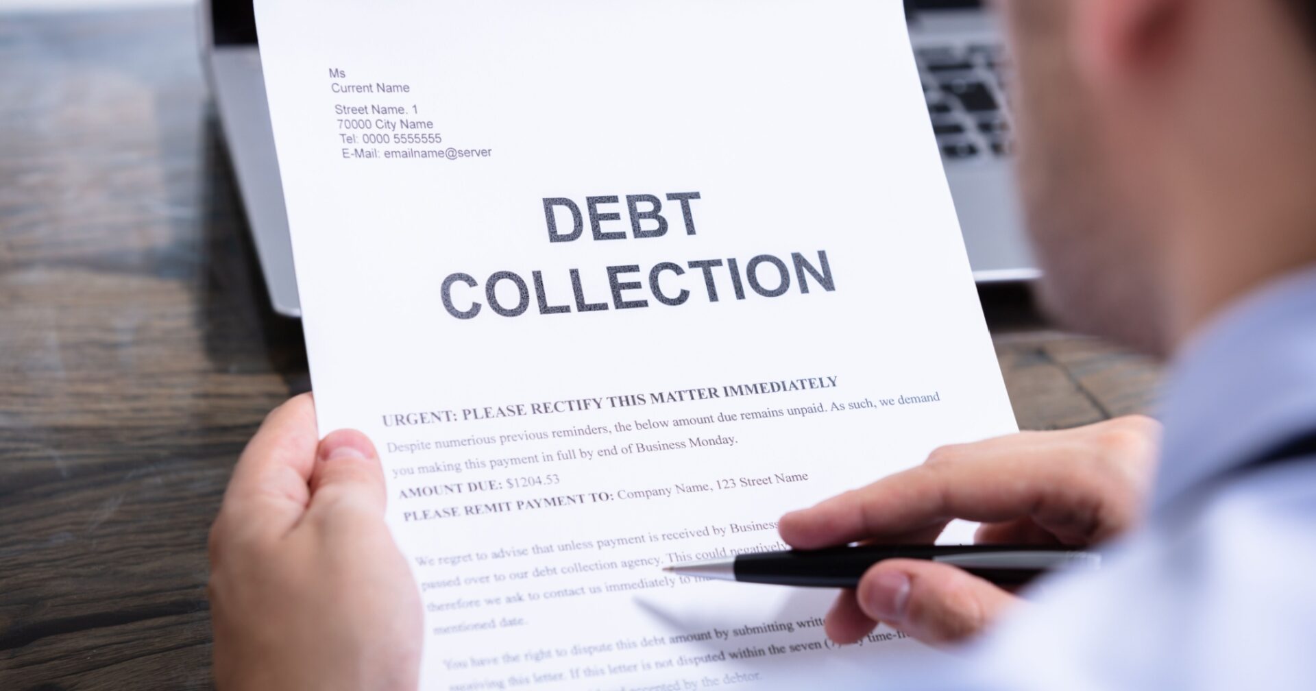 Person holding a debt collection notice in front of a laptop, with the words 'DEBT COLLECTION' prominently printed in bold at the top of the document.